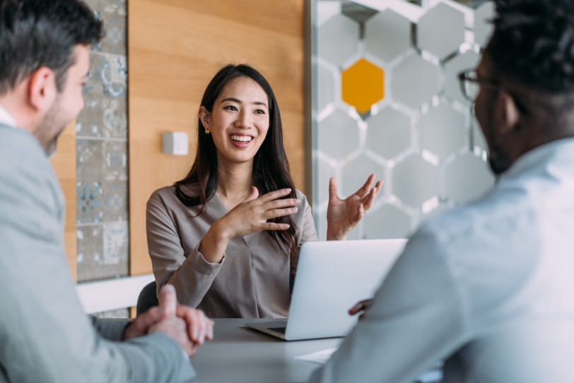 Asian woman in business meeting room speaking to a white man and black man
